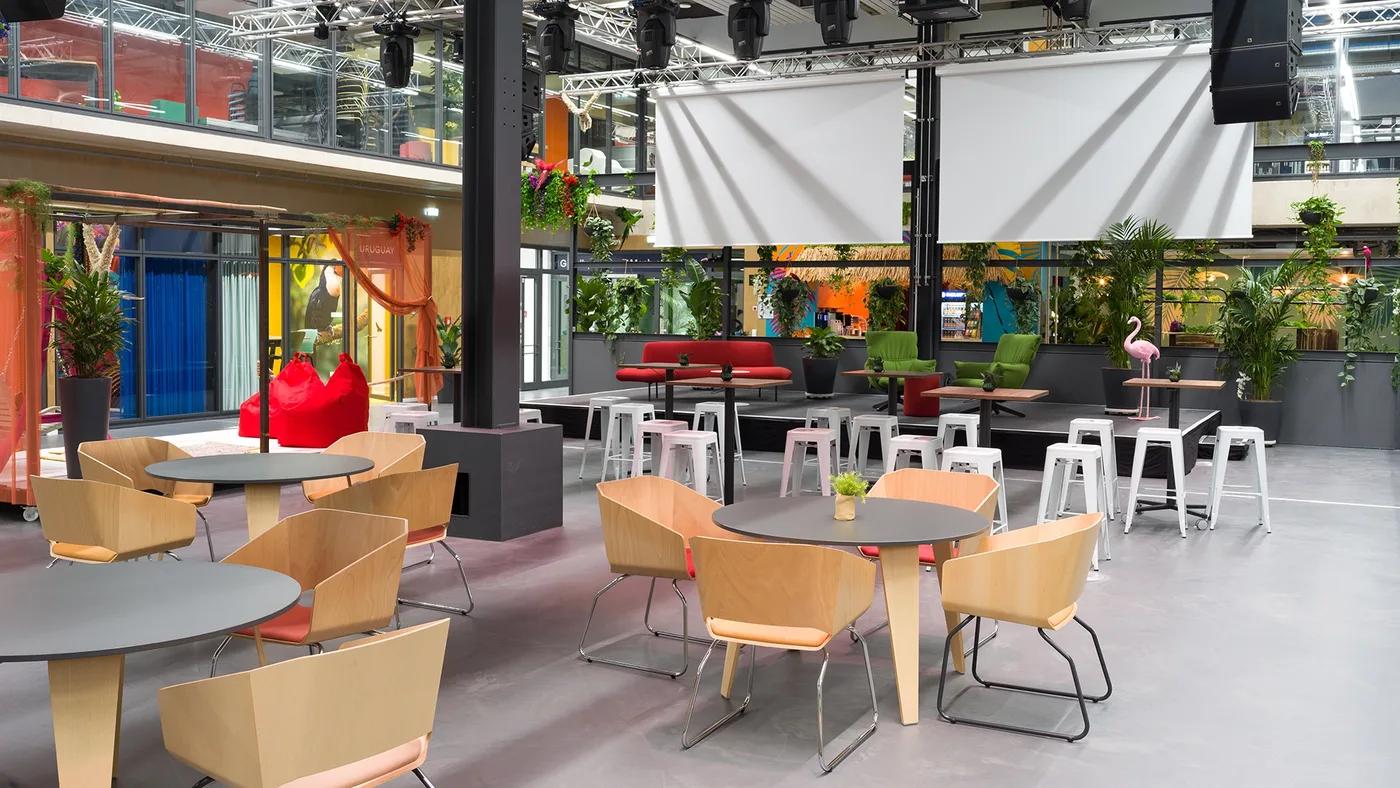 Event-Setup mit runden Tischen und zwei großen Leinwänden über der Bühne