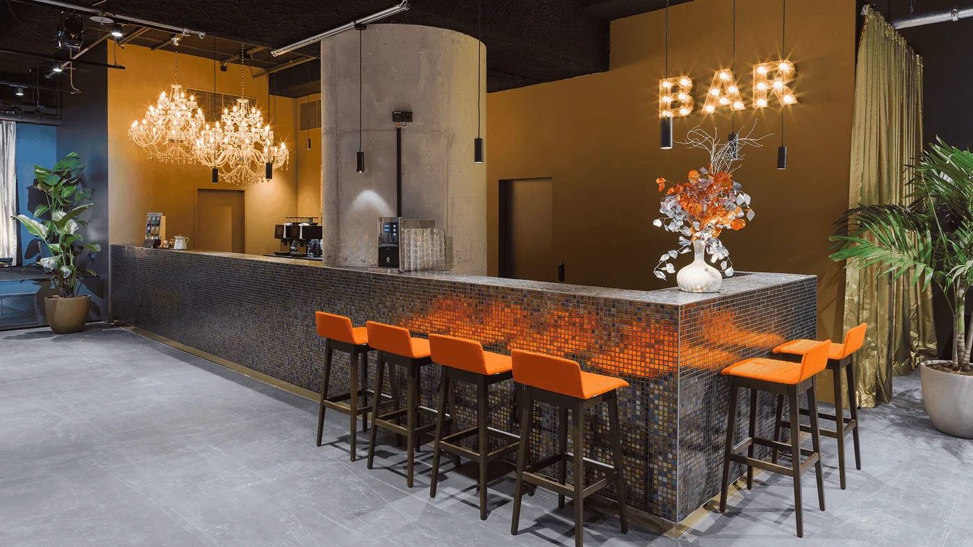 Die Mosaik-Bar im Detail: orange Barhocker und BAR-Leuchtbuchstaben