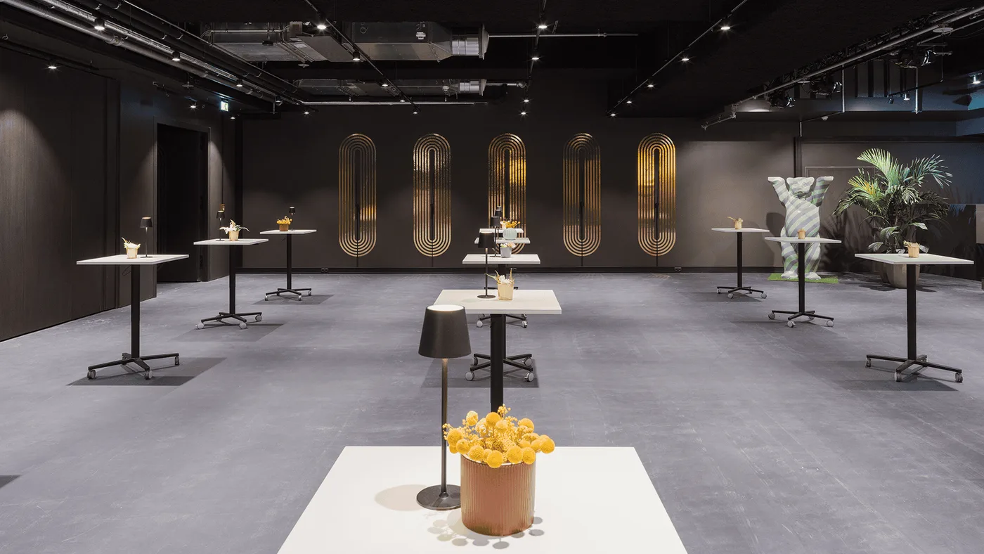 Stehtische mit Tischleuchten vor goldenen Art-déco-Ornamenten